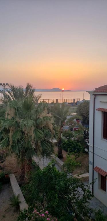 a sunset over the ocean with palm trees and a building at Home of sunset in Rethymno