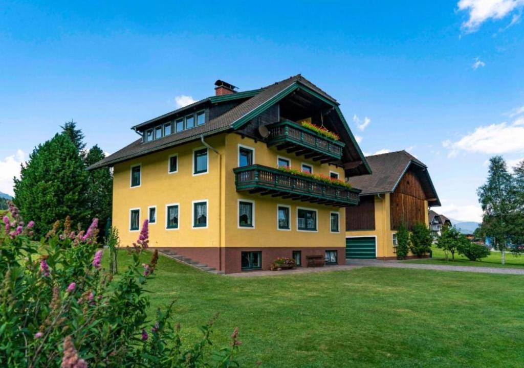 une grande maison jaune avec un balcon sur une pelouse dans l'établissement Appartement Lasshofer, à Mauterndorf