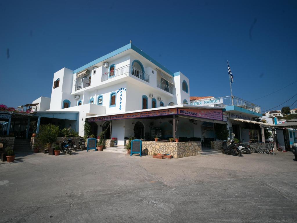 duży biały budynek z ludźmi siedzącymi poza nim w obiekcie Calypso Hotel w mieście Lipsi
