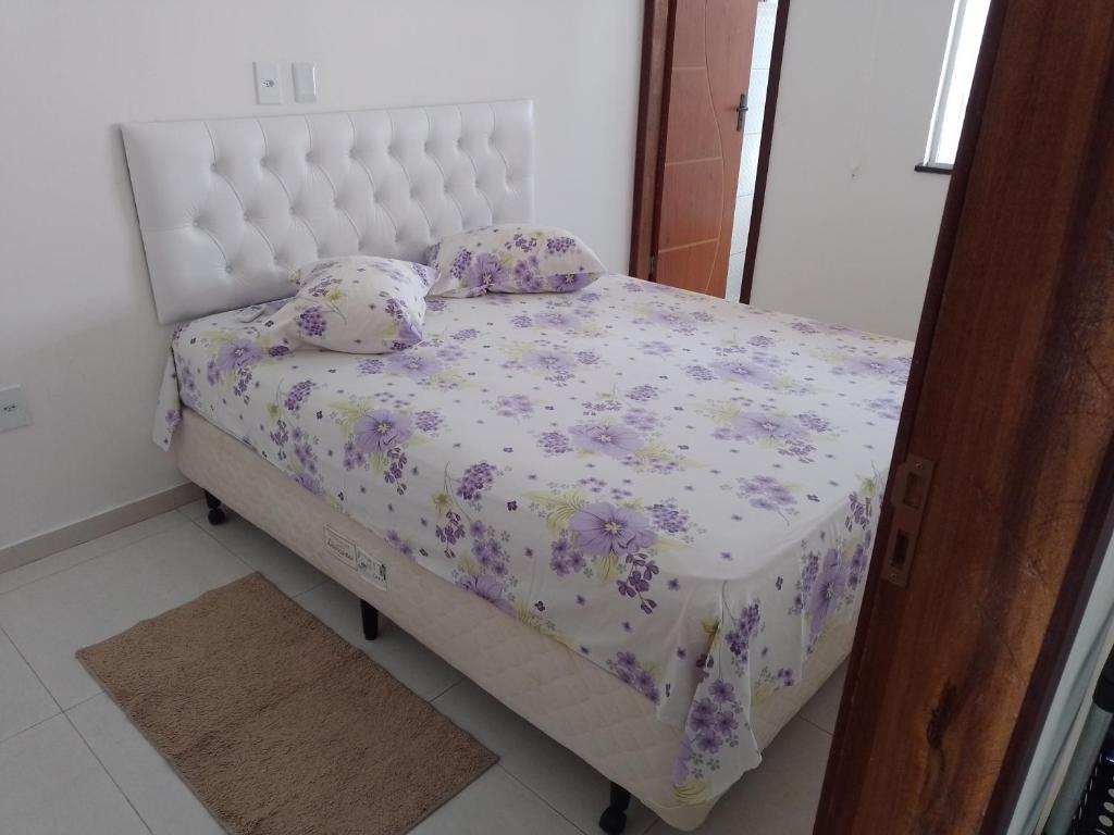 Cama pequeña en habitación con flores púrpuras en @vempraarembepe, en Camaçari