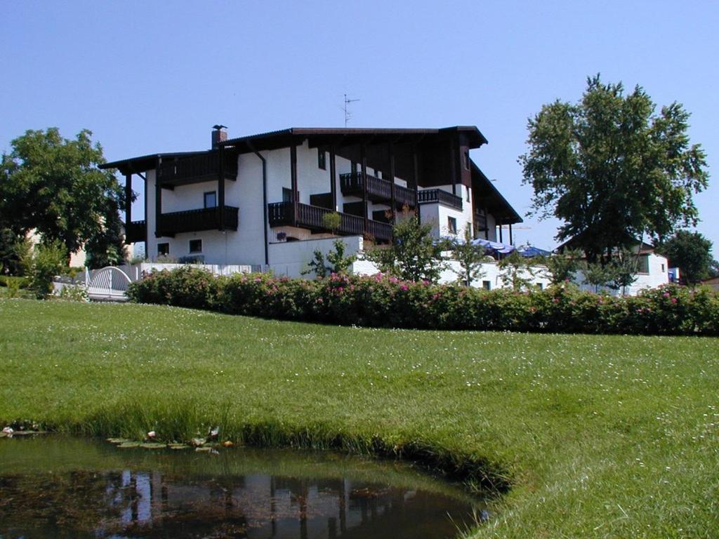 une maison sur une colline avec un étang en face de celle-ci dans l'établissement Kurhotel Würdinger Hof, à Bad Füssing