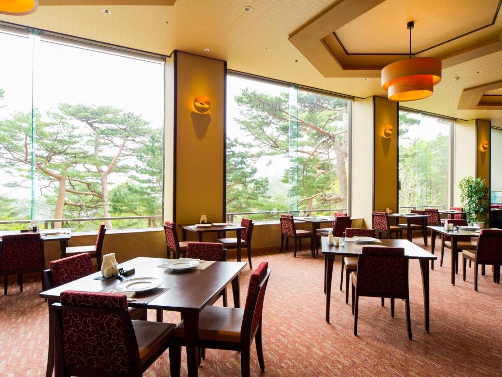 a restaurant with tables and chairs and large windows at Jodogahama Park Hotel in Miyako