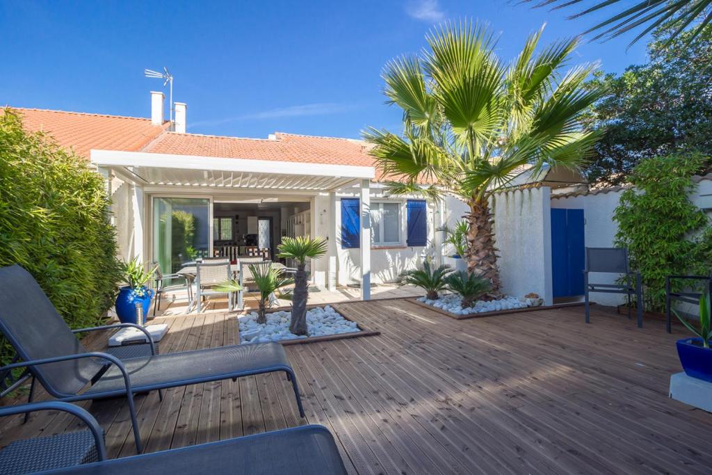 a wooden deck with palm trees and a house at VILLA LES PALMIERS in Palavas-les-Flots