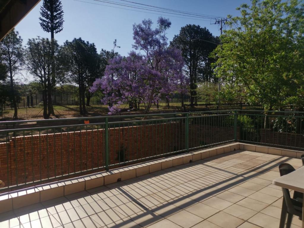 uma varanda com uma cerca e árvores com flores roxas em Rose Guest House em Pretoria
