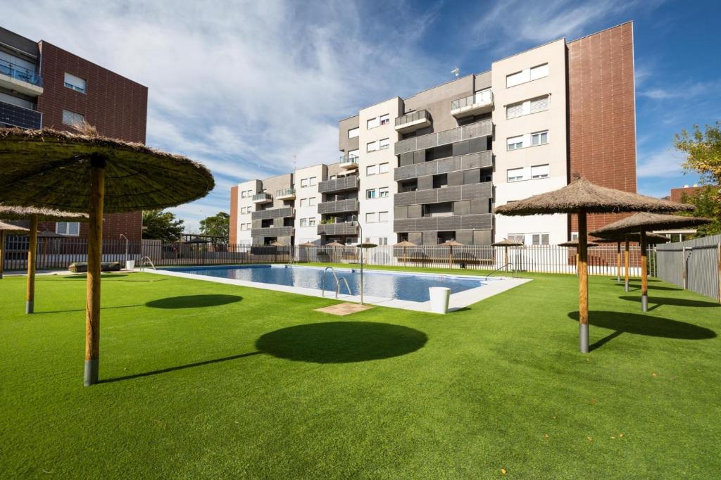 a courtyard with a swimming pool and umbrellas at Cómodo apartamento a pie de carretera in Alhendín