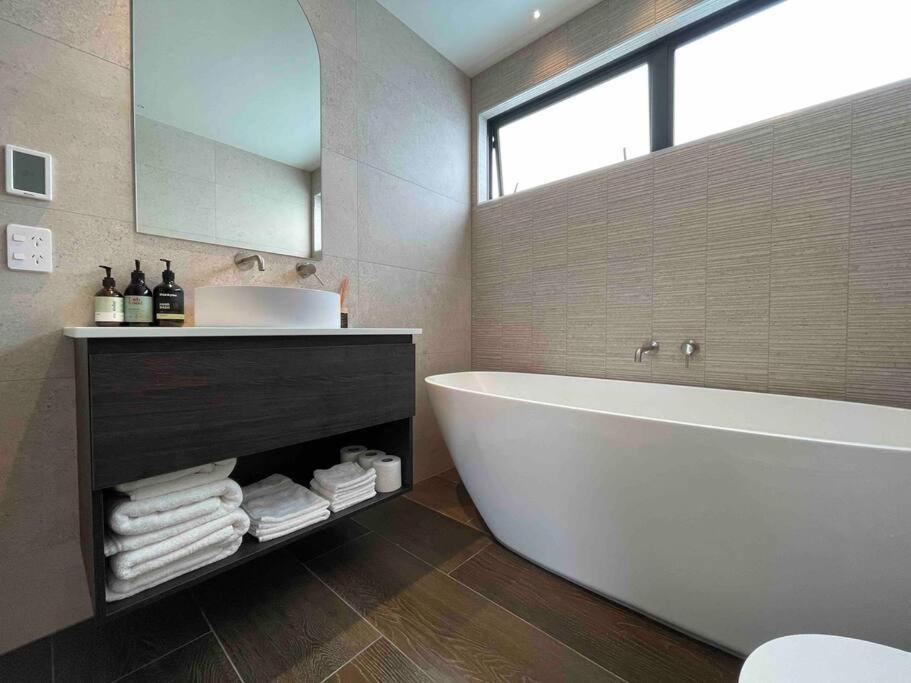 Luxury 3 Bedroom Home With Double Garage في كرايستشيرش: حمام مع حوض ومغسلة ومرآة
