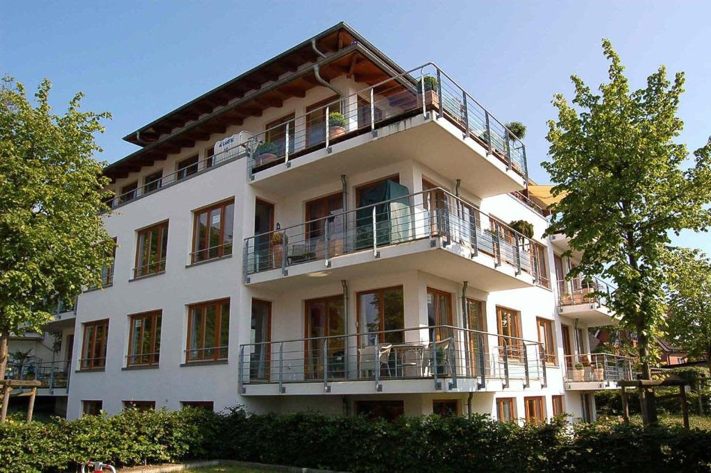 ein großes weißes Gebäude mit einem Balkon und Bäumen in der Unterkunft Haus am Strand Ferienwohnung Nr 01 in Niendorf