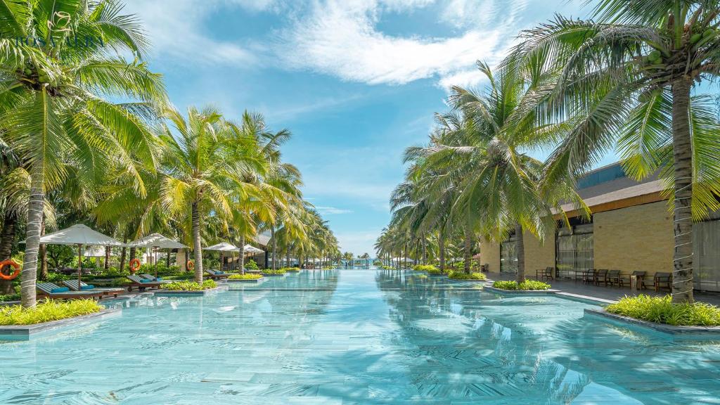 a swimming pool with palm trees in a resort at Rosa Alba Resort & Villas Tuy Hoa in Tuy Hoa