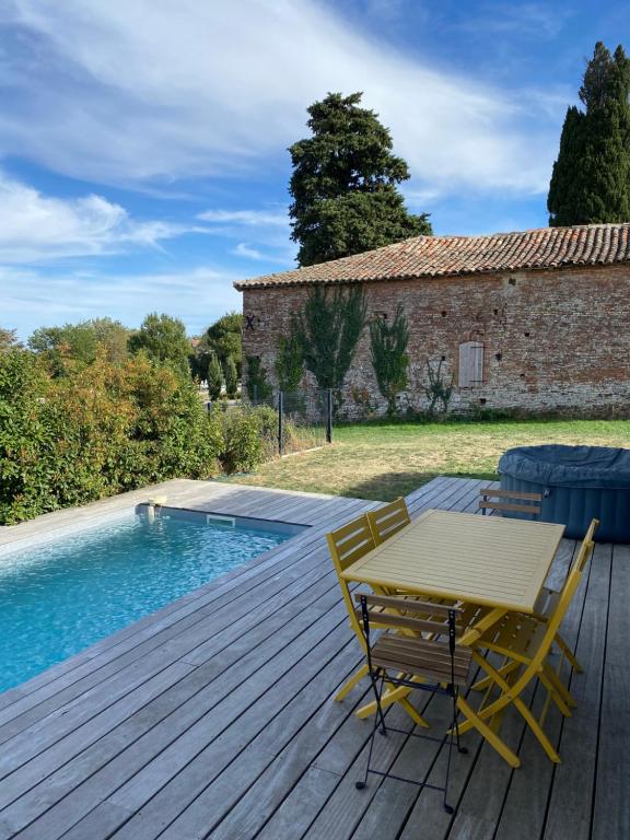 eine Holzterrasse mit einem Tisch und Stühlen neben einem Pool in der Unterkunft Magnifique villa avec piscine et spa in Saint-Jean-Lherm