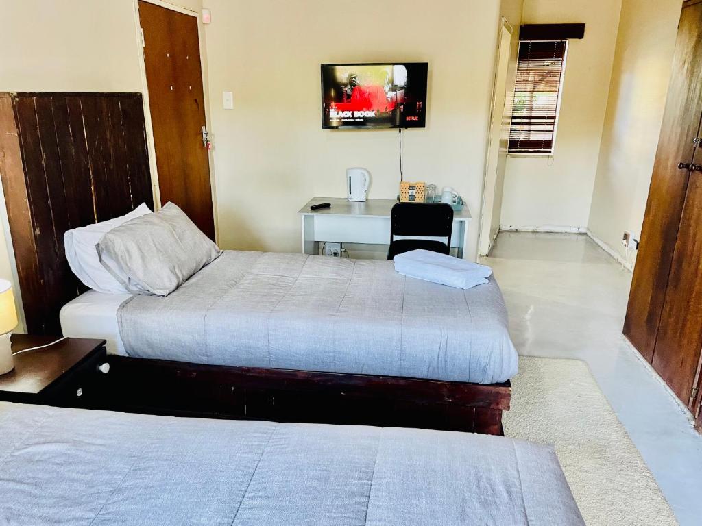 two beds in a room with a desk and a table at SapzRes at Klerksdorp in Klerksdorp