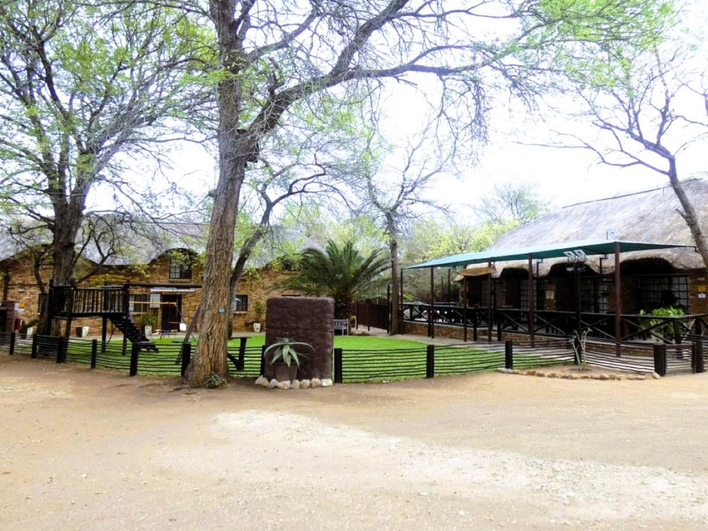 a park with a building and a tree and a fence at Weltevrede Lodge - Self Catering Houses in Marloth Park