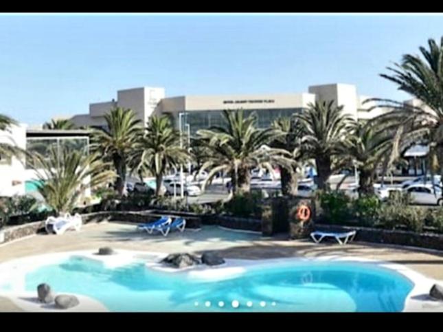 una gran piscina con palmeras y un edificio en Casa jablillo 2 en Costa Teguise