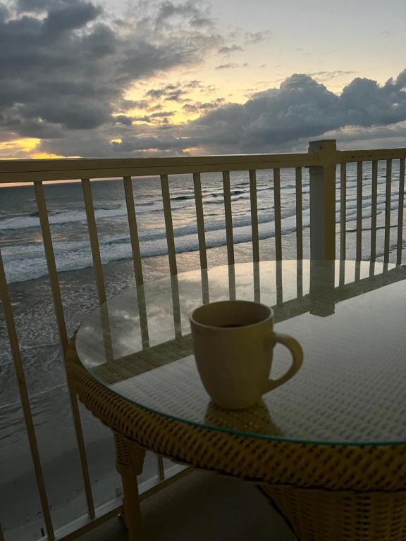 a coffee cup sitting on a table on a balcony overlooking the ocean at Ponce de Leon Towers in New Smyrna Beach