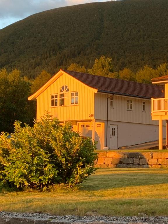 a yellow house with a mountain in the background at Sivert´s kontorhotell in Tomrefjord