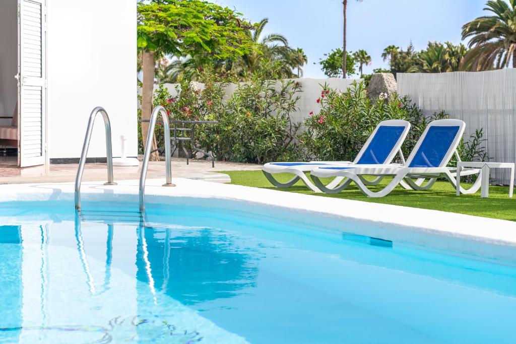 a swimming pool with two blue chairs next to it at Bungalows Las Almenas in Maspalomas