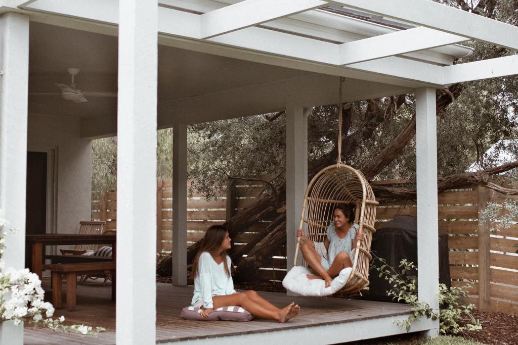 two women sitting on the porch of a porch swing at Verandah Retreat - A Beach House by the sea in Cowes