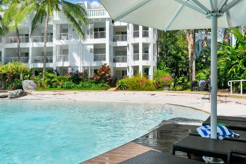 ein Pool mit Sonnenschirm neben einem Gebäude in der Unterkunft Private Ground Floor Apartment Beach Club Palm Cove in Palm Cove