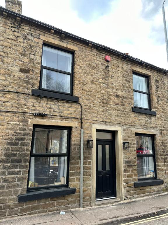 a brick building with three windows and a black door at Entire boutique mill cottage in Elland