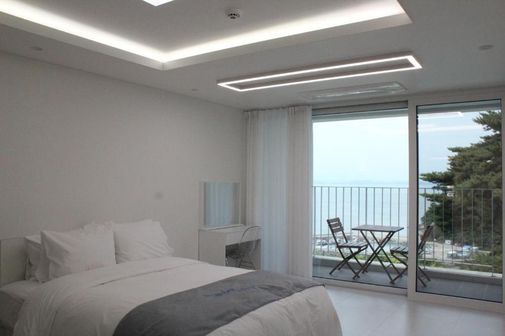 a white bedroom with a bed and a balcony at Vesper Namhae in Namhae