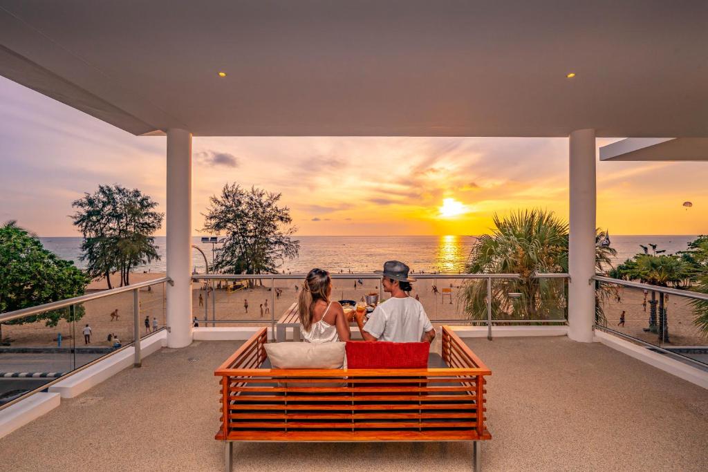 een man en vrouw die op een bank zitten en naar de zonsondergang kijken bij Paradox Resort Phuket - SHA Plus in Karon Beach