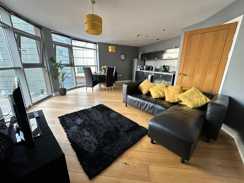 a living room with a black leather couch and a kitchen at Fantastic and modern city centre flat with FREE parking! in Cardiff