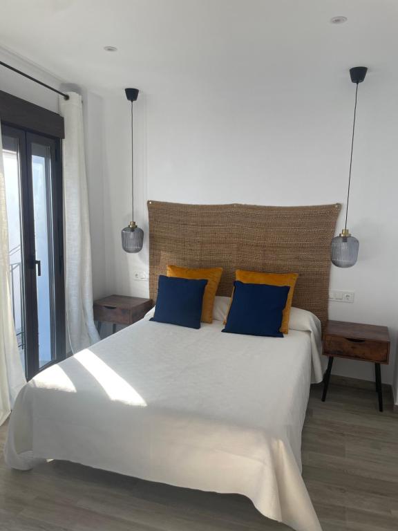 1 dormitorio con 1 cama blanca grande con almohadas azules en El Refugio, en Zahara de la Sierra