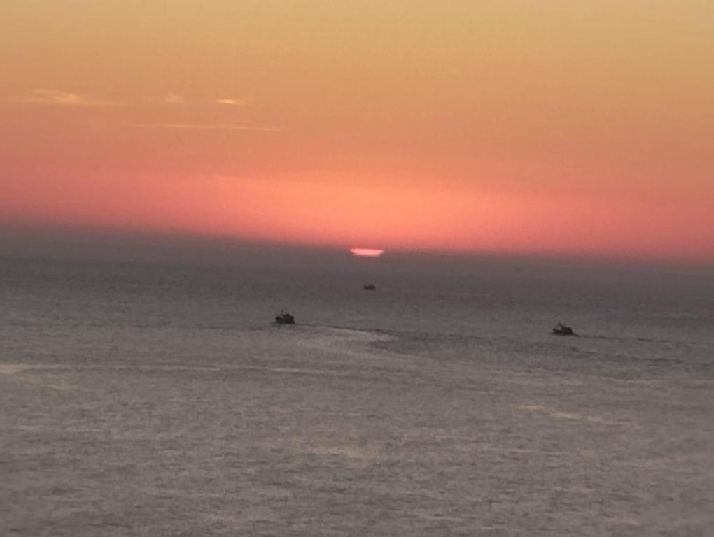 a sunset over the ocean with two boats in the water at AlMohit Larache in Larache