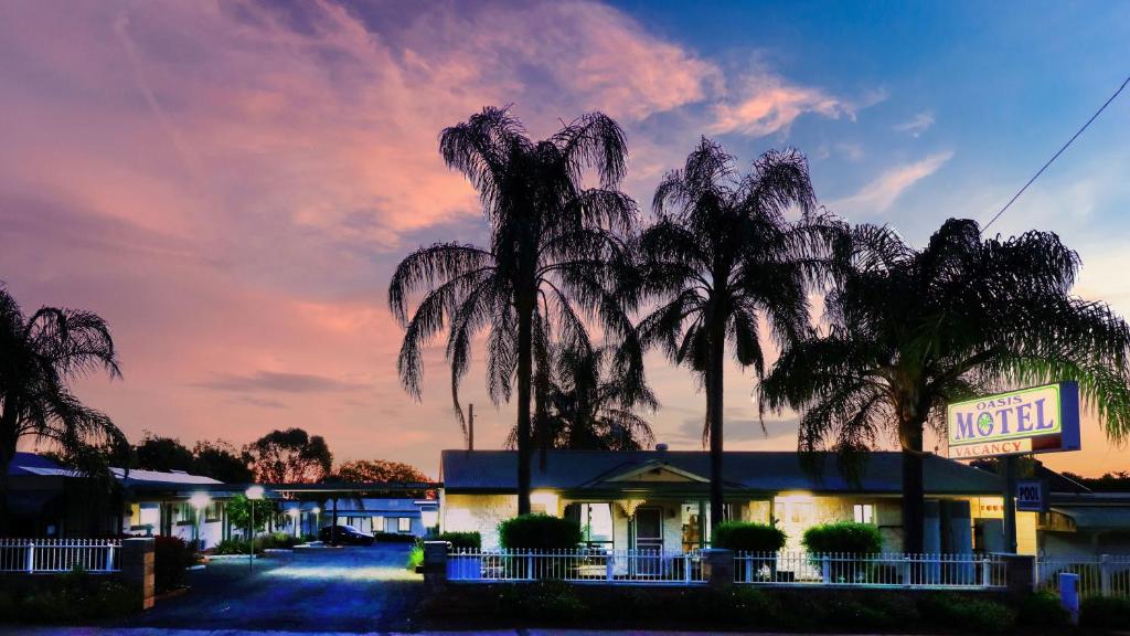 a motel with palm trees in front of a sunset at Oasis Motel in Peak Hill