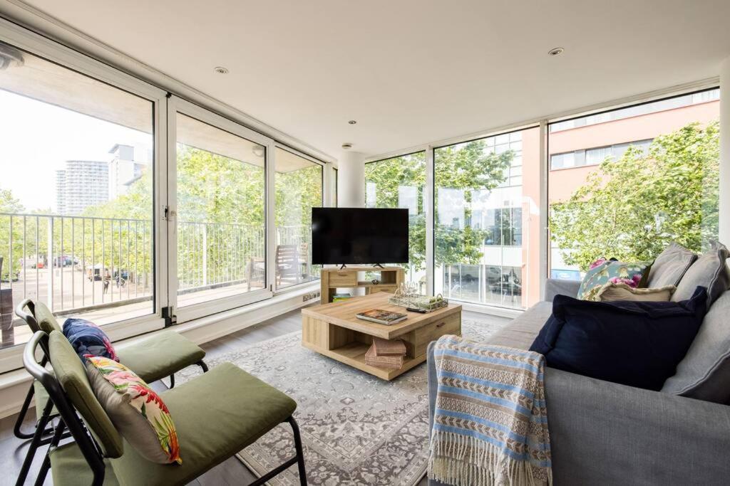 Convenient - ExCel London - O2- 3 Bedroom Apartment في لندن: غرفة معيشة مع أريكة وتلفزيون ونوافذ