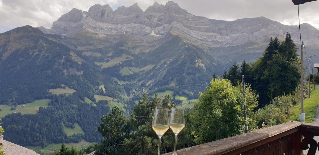 two wine glasses on a balcony with a view of mountains at Chalet le Grenier des Crosets, Vue exceptionnelle sur les Dents du Midi in Champéry