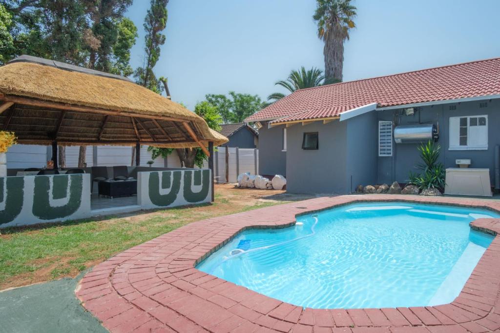 a swimming pool in front of a house with a straw umbrella at Home Life Guesthouse in Midrand