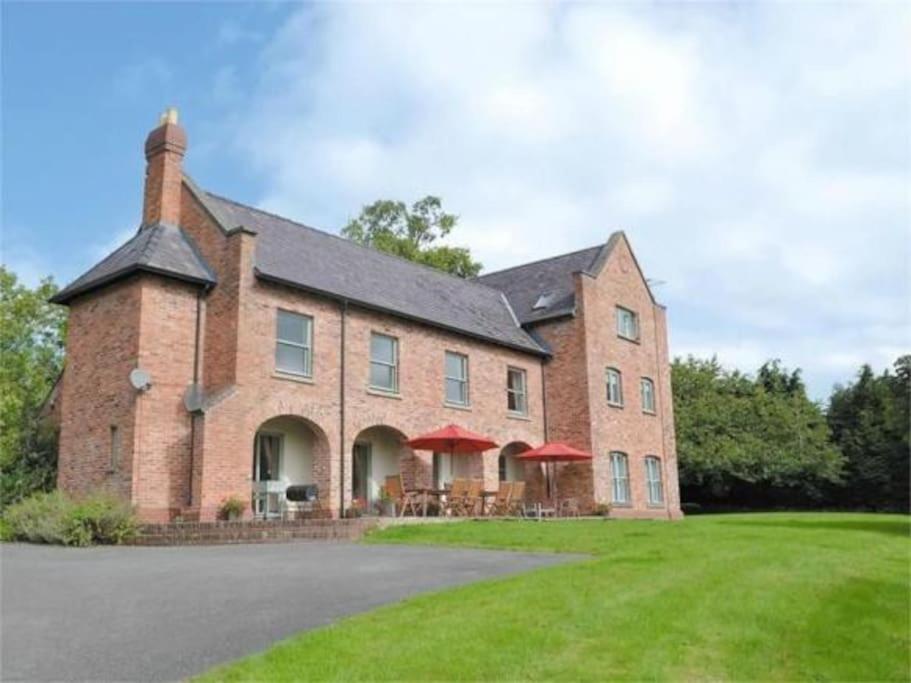 a large brick building with red umbrellas on a lawn at Gaer Hall Guilsfield a country mansion with hottub in Welshpool