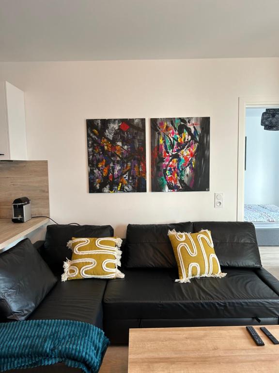 a black couch in a living room with two paintings at Chic &amp; moderne appartement - proximité métro in Asnières-sur-Seine