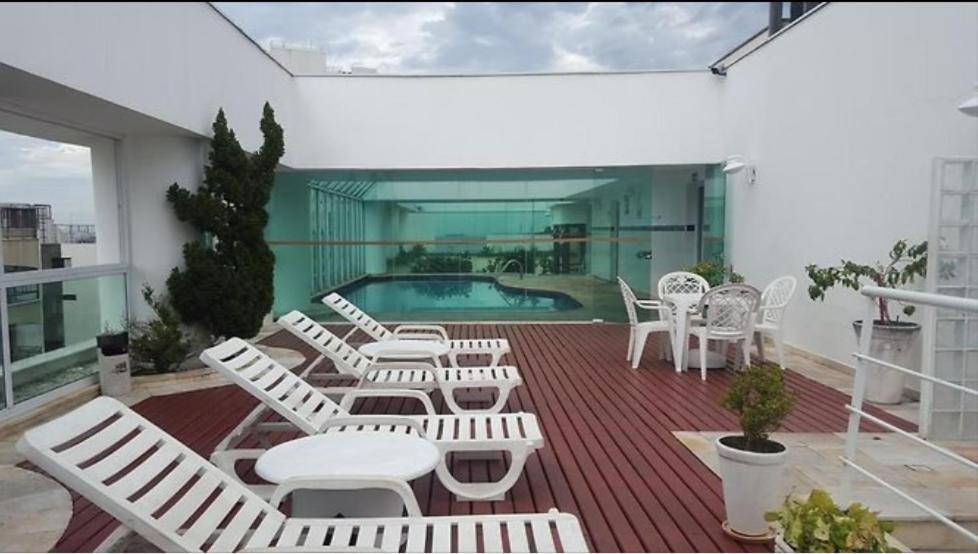 um deque com cadeiras brancas e uma piscina em Apartamento Flat pé na areia com piscina aquecida no Guarujá
