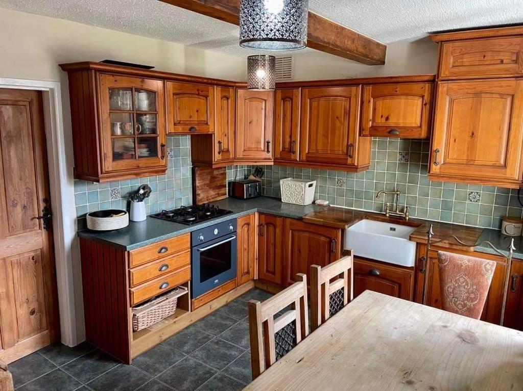 a kitchen with wooden cabinets and a stove top oven at Pilgrims Rest with Annexe in Cheddar