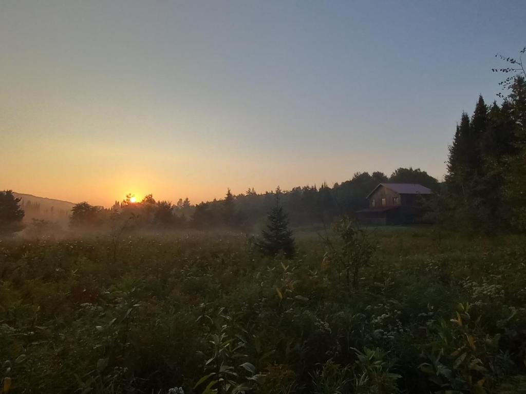 una puesta de sol en un campo con una casa en el fondo en Private Country Retreat on 80 acres 