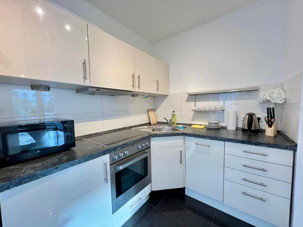 eine Küche mit weißen Schränken, einer Spüle und einer Mikrowelle in der Unterkunft Work&Stay Apartment - Kiel in Kiel