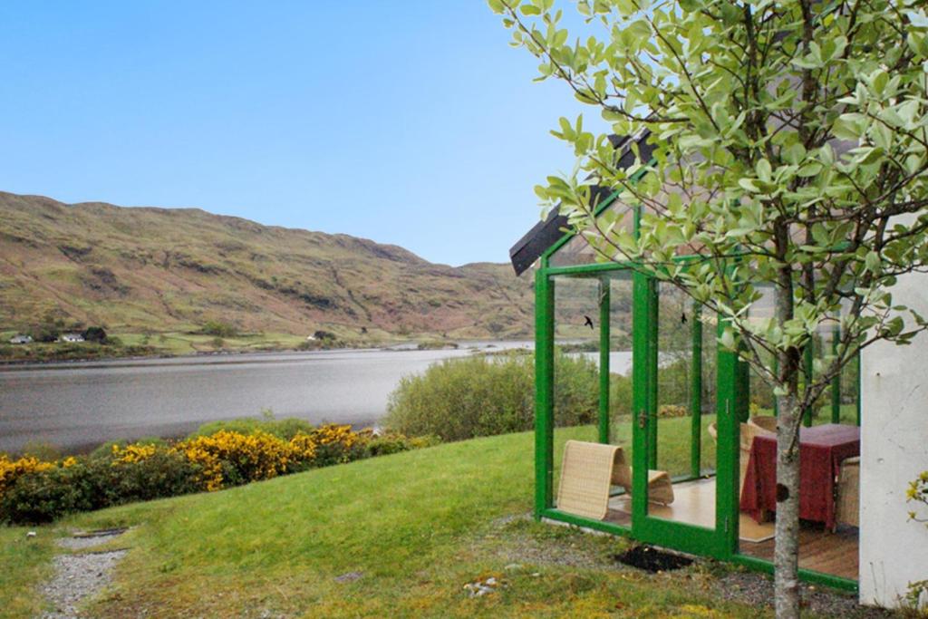 a green bench next to a tree next to a lake at One bedroom house with lake view and enclosed garden at Tourmakeady/Derrypark in Finny