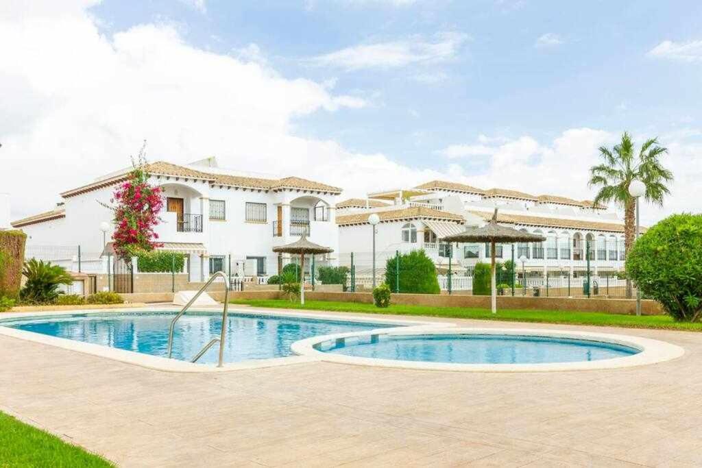 a villa with a swimming pool in front of a building at Bungalow Pink Punta Prima in Alicante