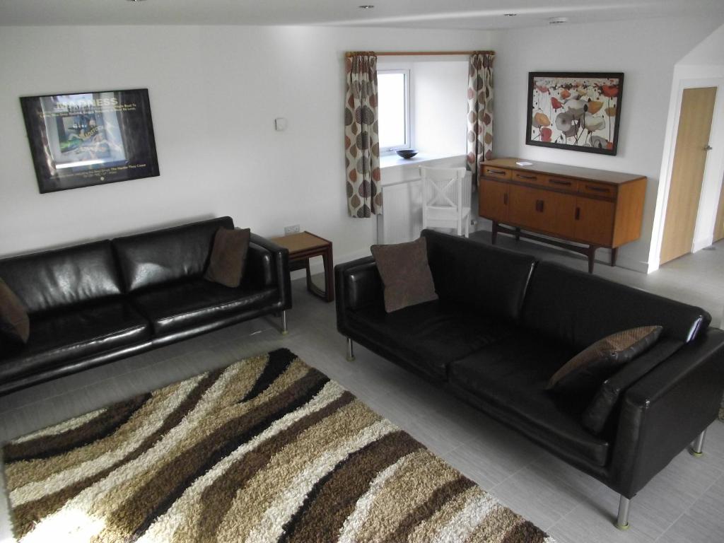 a living room with black leather couches and a rug at 6B Church St. Dingwall Apartment in Dingwall