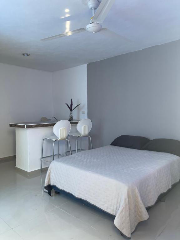a bedroom with a white bed and two chairs at Apartamentos Cupules in Mérida