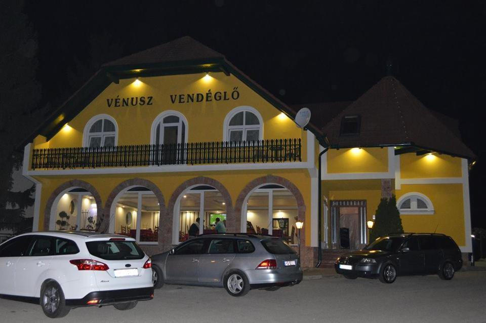 two cars parked in front of a yellow building at Vénusz Panzió és Vendéglő in Bagod