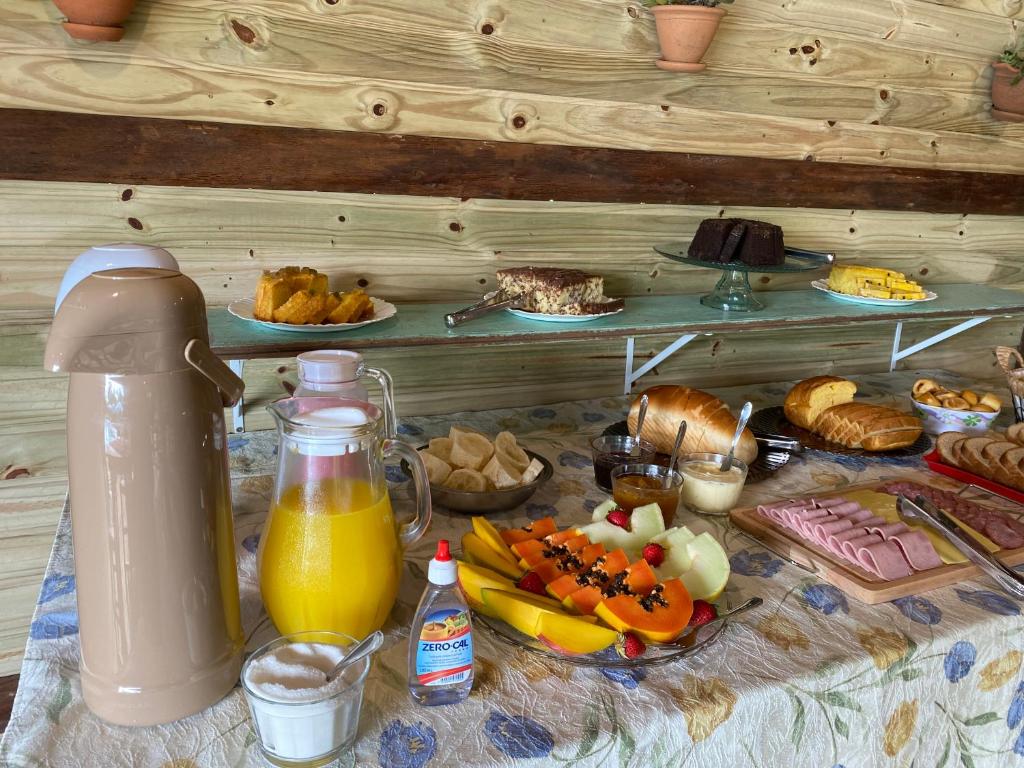 a table with breakfast foods and a jug of orange juice at Pousada & Camping Nativos dos Canyons in Praia Grande