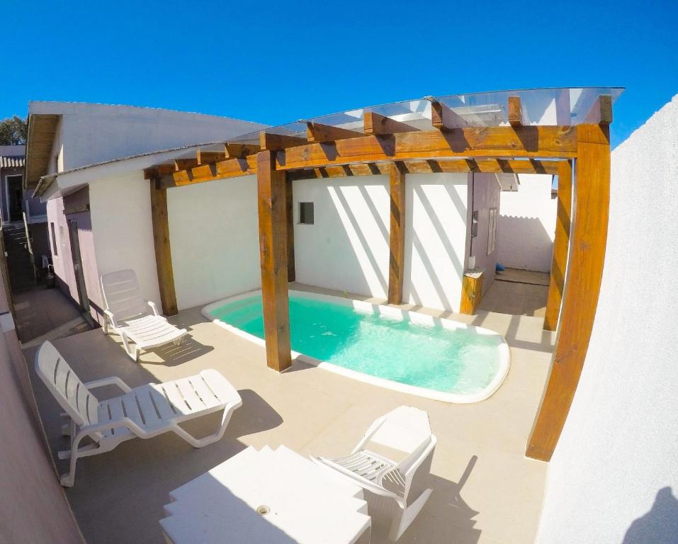 um pátio com uma piscina e cadeiras e uma pérgola em Residencial Viva Torres - Casas com 2 Dorms, Ar e Piscina Aquecida na Praia da Cal em Torres