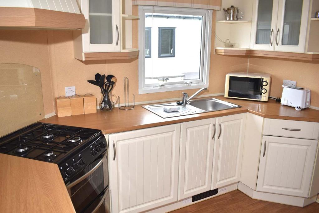 una cucina con armadi bianchi, lavandino e forno a microonde di Caprice Gold SU18 a Minehead
