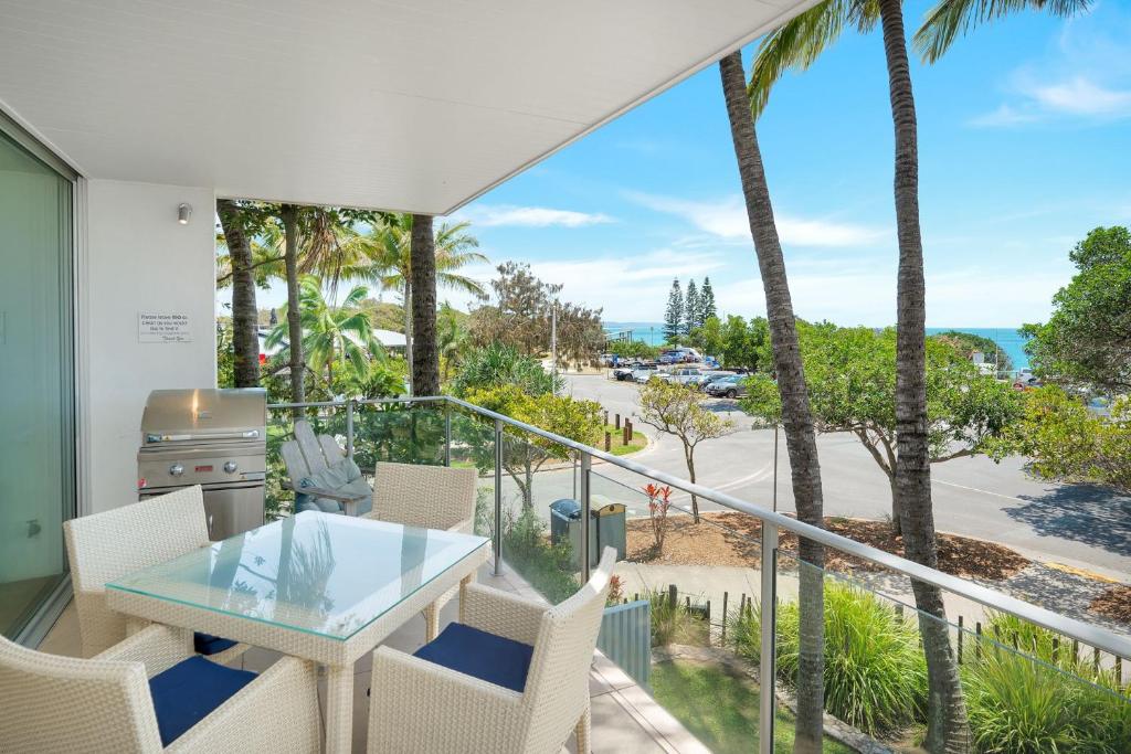d'un balcon avec une table en verre, des chaises et des palmiers. dans l'établissement Unit 105 Plantation Resort Rainbow Beach, à Rainbow Beach