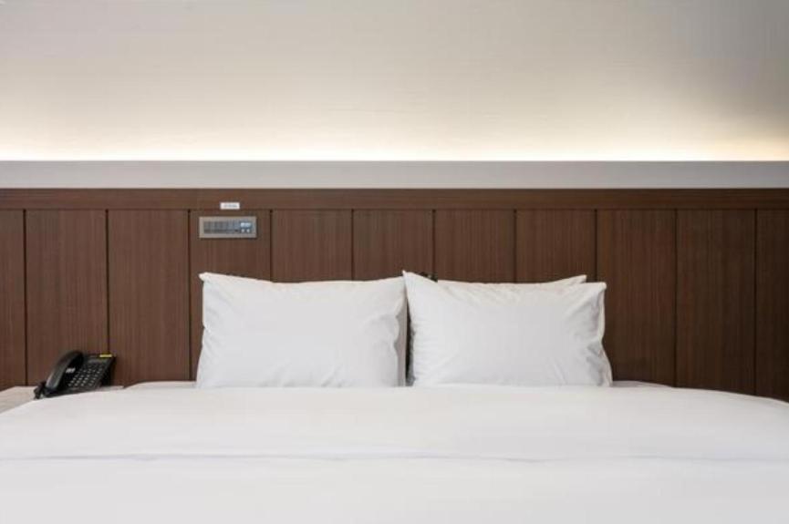 uma cama com lençóis e almofadas brancos e um telefone em Hotel Harbor em Tongyeong