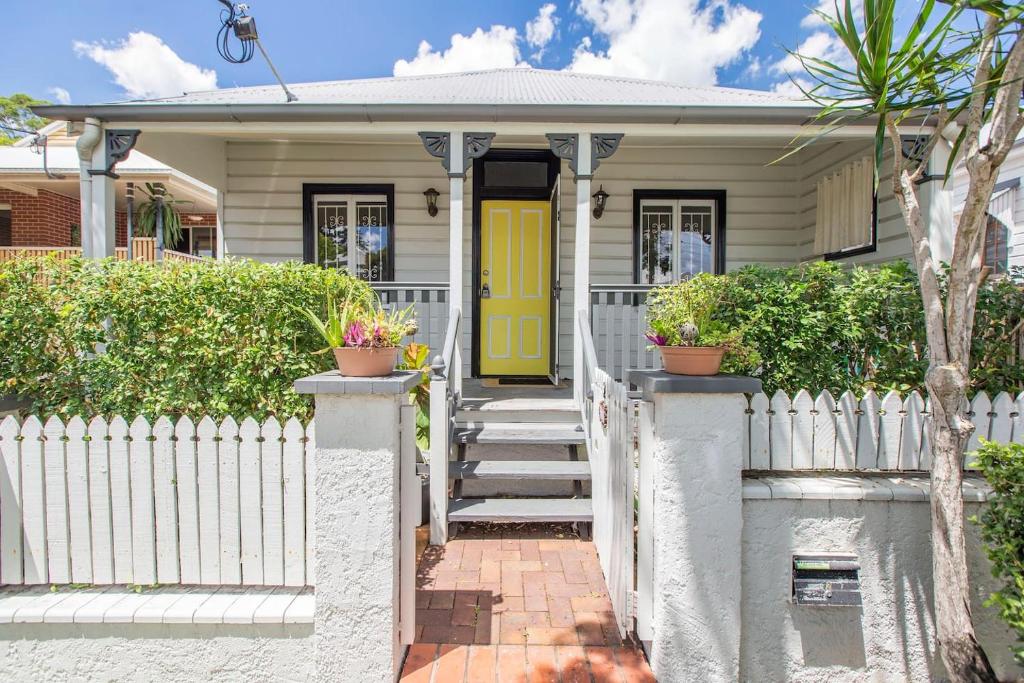 a house with a yellow door and a white fence at Fernberg Cottage - Sunny Queenslander Charm in Brisbane