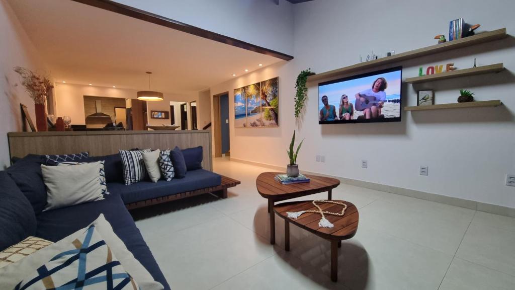 ein Wohnzimmer mit einem blauen Sofa und einem TV an der Wand in der Unterkunft Confortável Casa de Praia em Itacimirim - 04 SUÍTES in Itacimirim