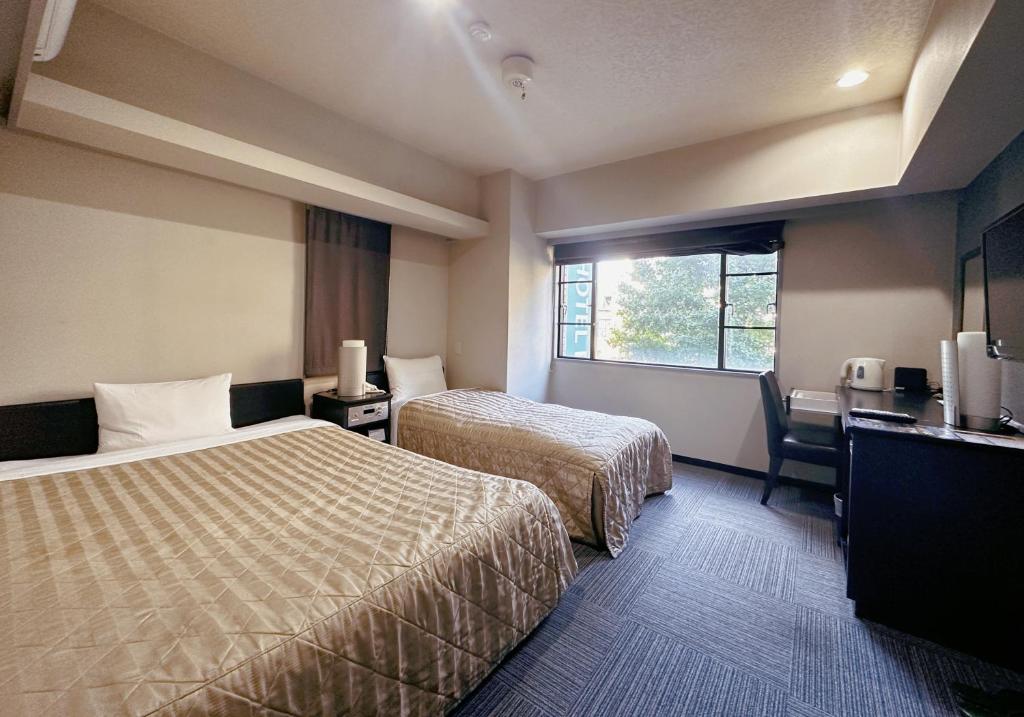 a hotel room with two beds and a desk and a window at Nissei Hotel Fukuoka in Fukuoka